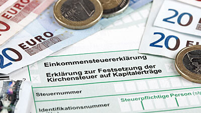 Geldscheine und Münzen liegen auf einem Formular für die Steuererklärung.