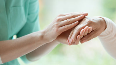 Palliativpflegerin haelt eine alte Hand